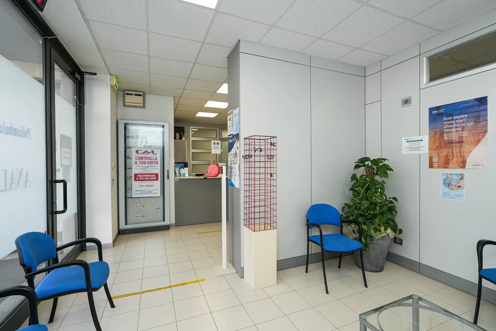 Accoglienza del poliambulatorio Vielle: sedute blu lungo il corridoio, bancone della reception sul fondo e area del punto prelievi Synlab